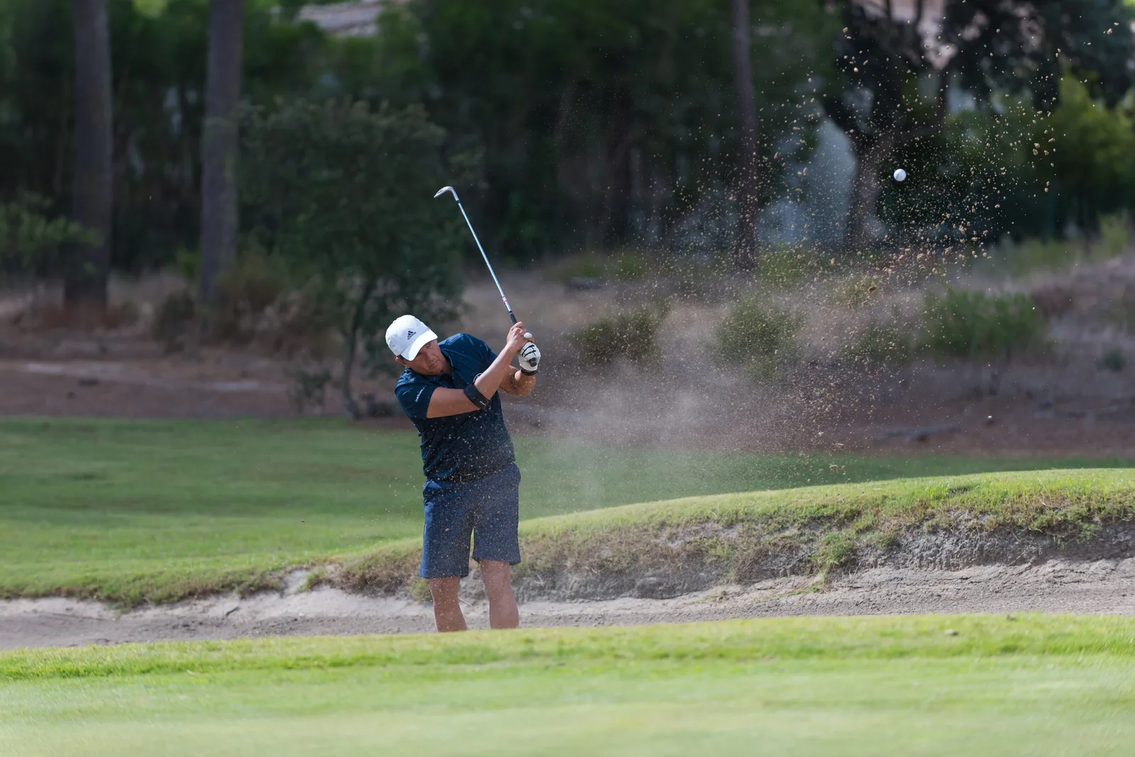 Golfista a sair do bunker numa nuvem de areia